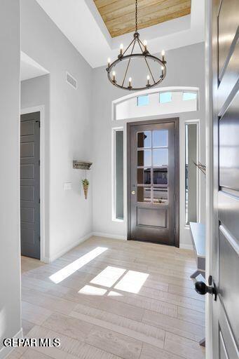 foyer entrance featuring a notable chandelier, wood ceiling, a tray ceiling, and light hardwood / wood-style floors