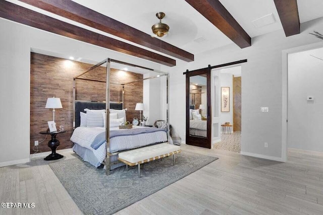 bedroom featuring a barn door, beamed ceiling, light wood-type flooring, ceiling fan, and wooden walls