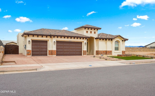 view of front facade featuring stucco siding, driveway, a gate, stone siding, and a garage