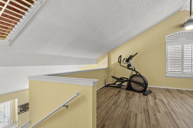 workout room featuring hardwood / wood-style flooring, lofted ceiling, and a textured ceiling