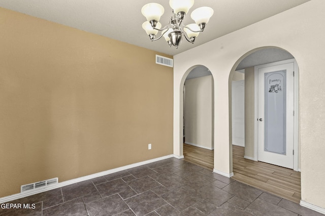 spare room featuring an inviting chandelier and dark hardwood / wood-style floors