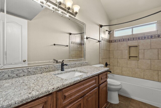 full bathroom with vaulted ceiling, tile patterned floors, vanity, tiled shower / bath, and toilet