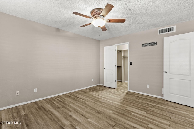 unfurnished bedroom featuring ceiling fan, a textured ceiling, light hardwood / wood-style flooring, and a walk in closet