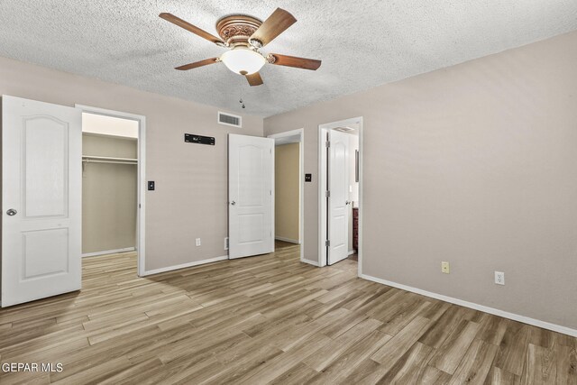 unfurnished bedroom with light hardwood / wood-style floors, a spacious closet, a closet, a textured ceiling, and ceiling fan