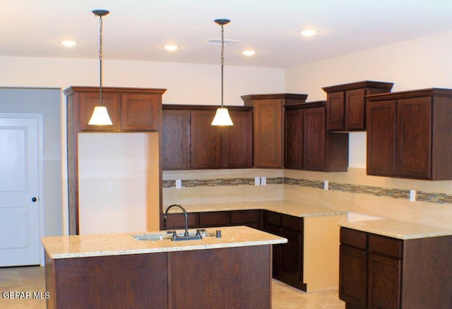 kitchen featuring decorative backsplash, a kitchen island with sink, sink, and hanging light fixtures