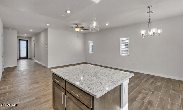 kitchen featuring pendant lighting, ceiling fan with notable chandelier, a kitchen island, hardwood / wood-style floors, and light stone countertops