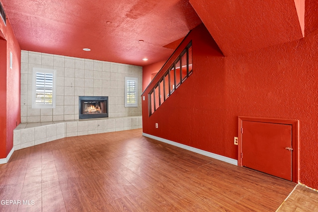 unfurnished living room featuring hardwood / wood-style flooring, a tiled fireplace, and a textured ceiling