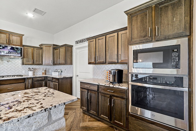 kitchen with light stone countertops, decorative backsplash, dark parquet floors, and appliances with stainless steel finishes