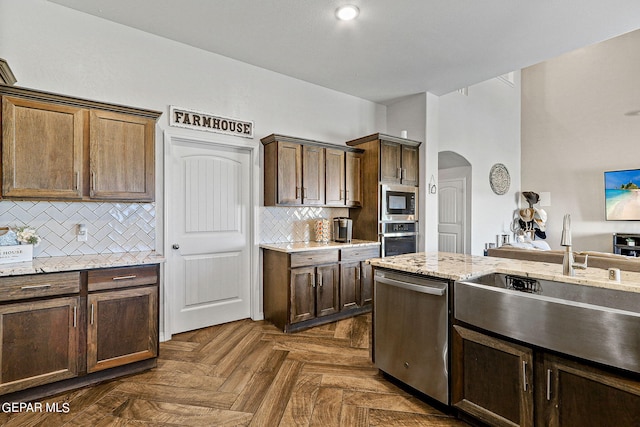 kitchen featuring light stone counters, sink, backsplash, appliances with stainless steel finishes, and dark parquet flooring