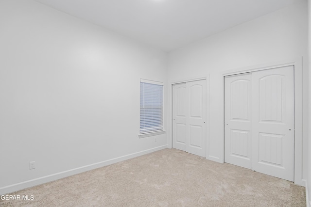 unfurnished bedroom featuring multiple closets and light colored carpet