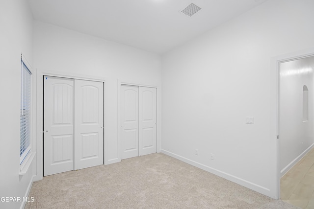 unfurnished bedroom with two closets and light colored carpet