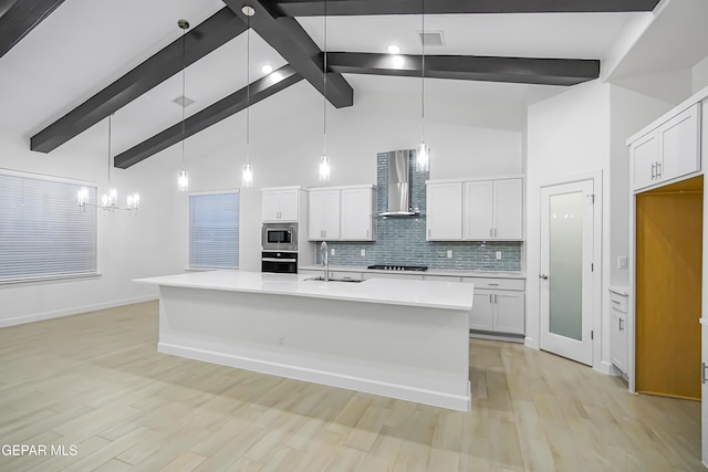 kitchen featuring wall chimney exhaust hood, decorative light fixtures, an island with sink, stainless steel appliances, and white cabinets