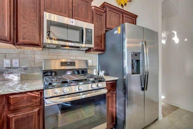 kitchen featuring stainless steel appliances, light stone counters, light tile patterned flooring, and tasteful backsplash