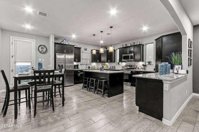 kitchen featuring appliances with stainless steel finishes, hanging light fixtures, kitchen peninsula, light wood-type flooring, and a kitchen bar