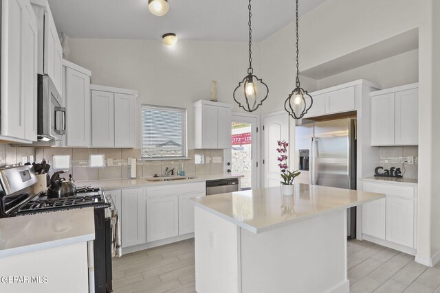 kitchen with a kitchen island, backsplash, white cabinetry, appliances with stainless steel finishes, and vaulted ceiling