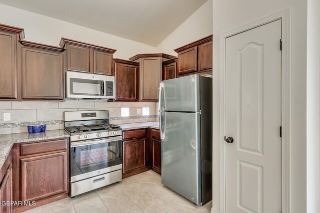 kitchen featuring appliances with stainless steel finishes, light tile patterned flooring, vaulted ceiling, backsplash, and light stone countertops