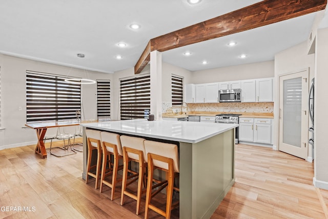 kitchen featuring a breakfast bar, white cabinetry, appliances with stainless steel finishes, and light hardwood / wood-style flooring