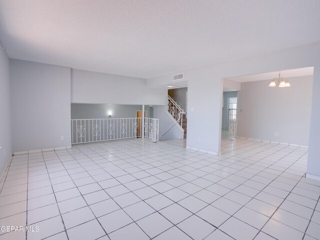 spare room featuring a notable chandelier, a textured ceiling, and light tile patterned floors