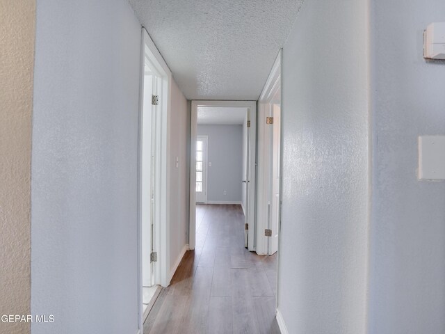 hallway with a textured ceiling and light hardwood / wood-style floors