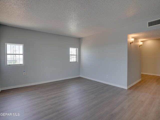 unfurnished room with a textured ceiling, light hardwood / wood-style floors, and plenty of natural light