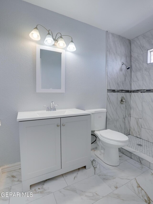 bathroom featuring a tile shower, vanity, and toilet