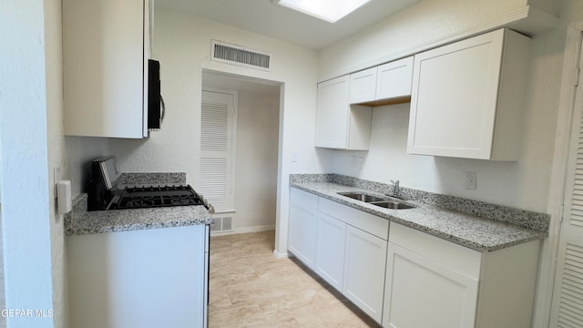 kitchen featuring light stone countertops, white cabinetry, and sink