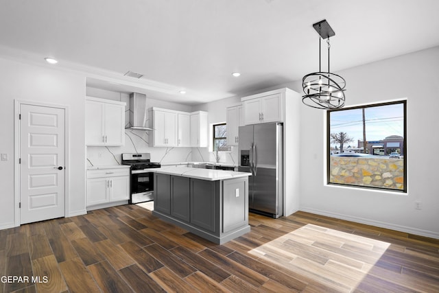 kitchen featuring wall chimney range hood, appliances with stainless steel finishes, hanging light fixtures, a center island, and white cabinets