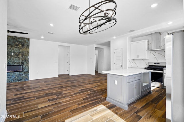 kitchen with wall chimney exhaust hood, light stone counters, a center island, hanging light fixtures, and stainless steel appliances