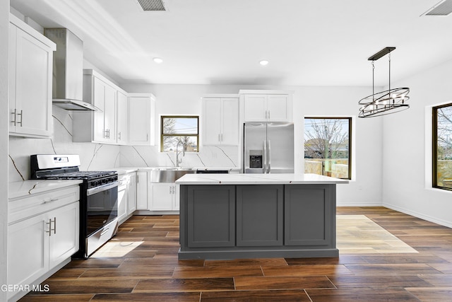 kitchen featuring pendant lighting, white cabinetry, stainless steel appliances, a center island, and wall chimney exhaust hood