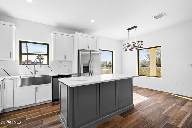 kitchen with a kitchen island, appliances with stainless steel finishes, white cabinets, and decorative light fixtures