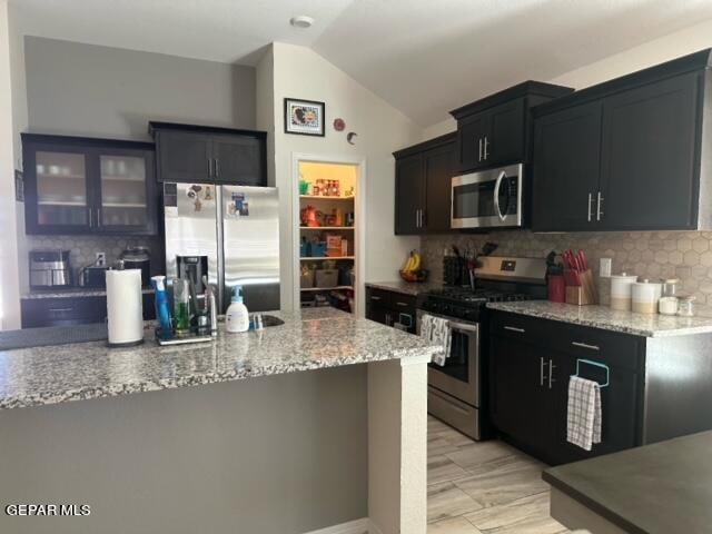 kitchen featuring light stone countertops, stainless steel appliances, vaulted ceiling, and backsplash