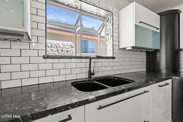 kitchen with white cabinets, backsplash, dark stone countertops, and sink