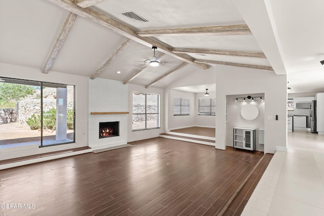 unfurnished living room featuring lofted ceiling with beams, a brick fireplace, ceiling fan, and dark hardwood / wood-style floors