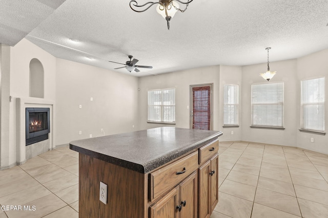 kitchen with a textured ceiling, a kitchen island, light tile patterned floors, decorative light fixtures, and ceiling fan