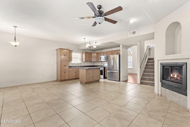 kitchen with ceiling fan with notable chandelier, a kitchen island, stainless steel appliances, decorative light fixtures, and sink