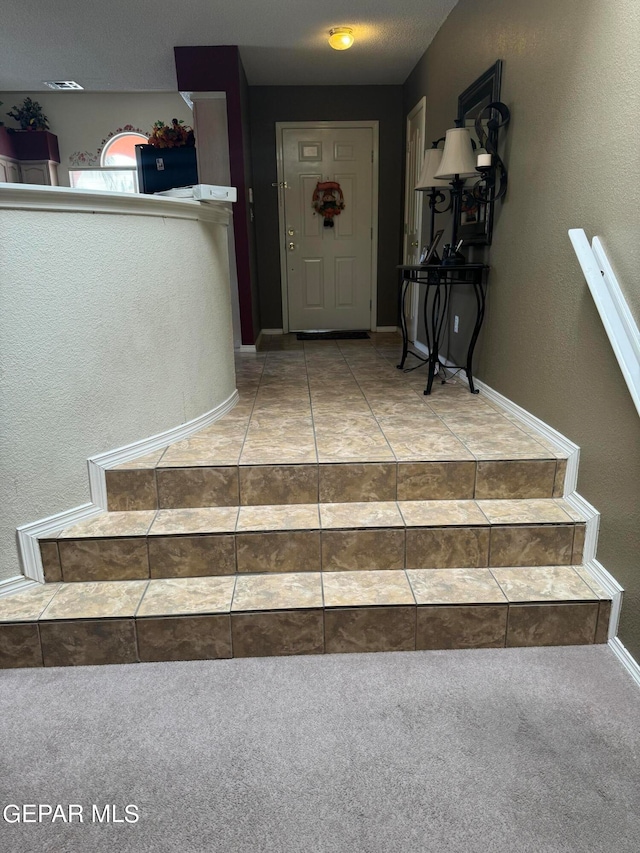 stairs featuring a textured ceiling and carpet flooring