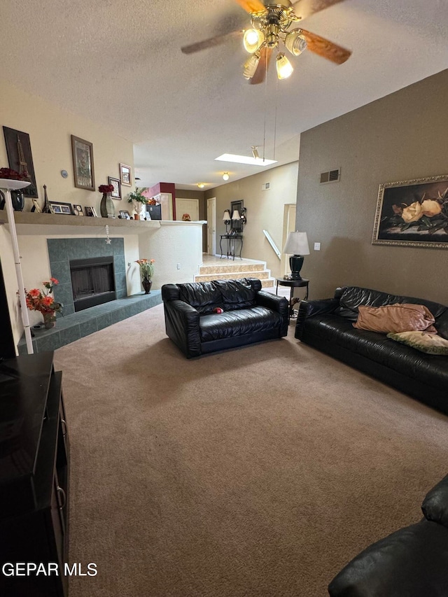 carpeted living room featuring ceiling fan, a tile fireplace, and a textured ceiling