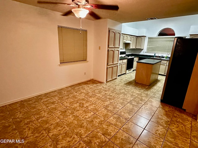 kitchen with white gas range oven, black fridge, sink, a kitchen island, and ceiling fan