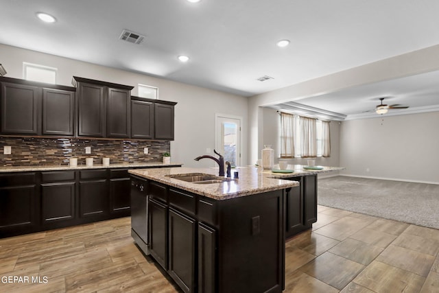 kitchen featuring decorative backsplash, ceiling fan, a center island with sink, sink, and light carpet