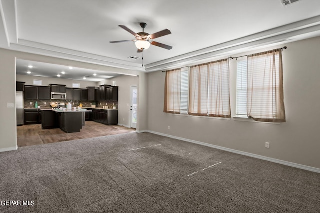 unfurnished living room featuring dark colored carpet, ceiling fan, and a raised ceiling