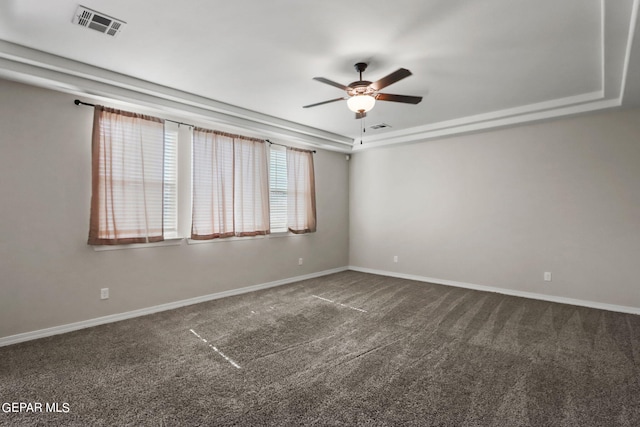 empty room with dark colored carpet, ceiling fan, and a raised ceiling