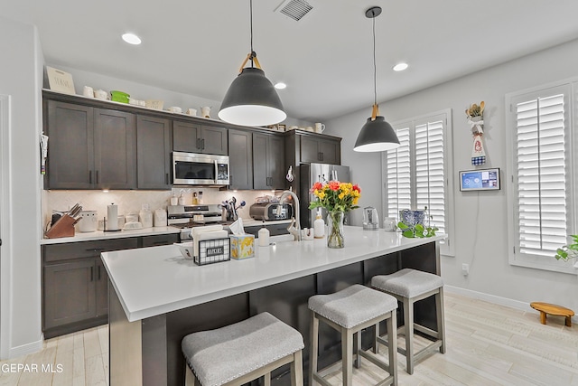 kitchen featuring dark brown cabinetry, pendant lighting, tasteful backsplash, light hardwood / wood-style flooring, and stainless steel appliances