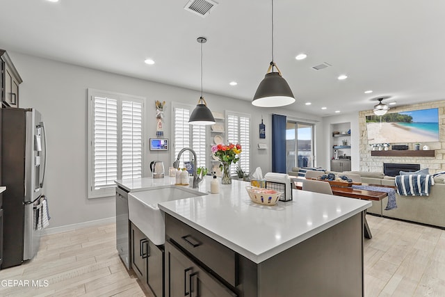 kitchen with pendant lighting, an island with sink, a stone fireplace, appliances with stainless steel finishes, and light wood-type flooring