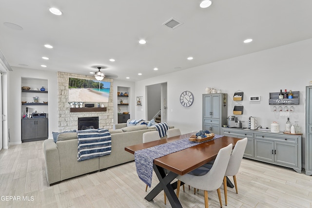 dining area featuring light hardwood / wood-style flooring, ceiling fan, a fireplace, and built in features