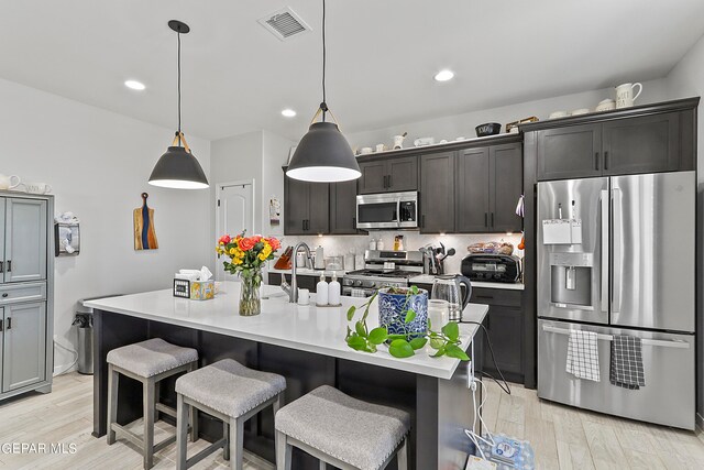 kitchen with light hardwood / wood-style floors, a kitchen island with sink, a breakfast bar area, hanging light fixtures, and appliances with stainless steel finishes