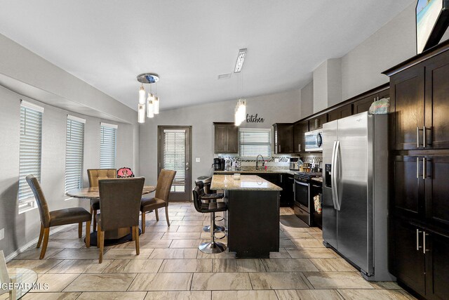 kitchen with light stone counters, stainless steel appliances, lofted ceiling, a center island, and decorative light fixtures