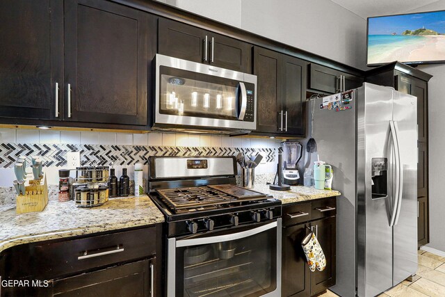 kitchen with dark brown cabinetry, light stone countertops, stainless steel appliances, and backsplash