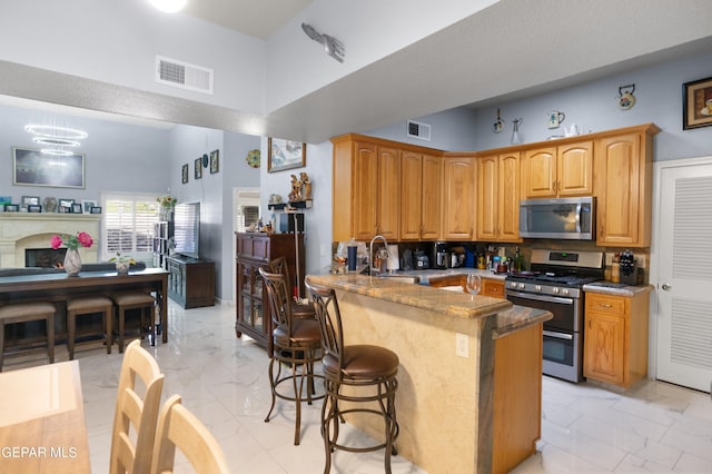 kitchen featuring sink, kitchen peninsula, a kitchen bar, stainless steel appliances, and a towering ceiling