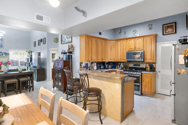 kitchen with a towering ceiling, a breakfast bar, kitchen peninsula, light stone countertops, and stainless steel appliances