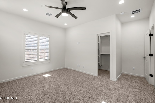 unfurnished bedroom featuring a closet, light colored carpet, ceiling fan, and a walk in closet